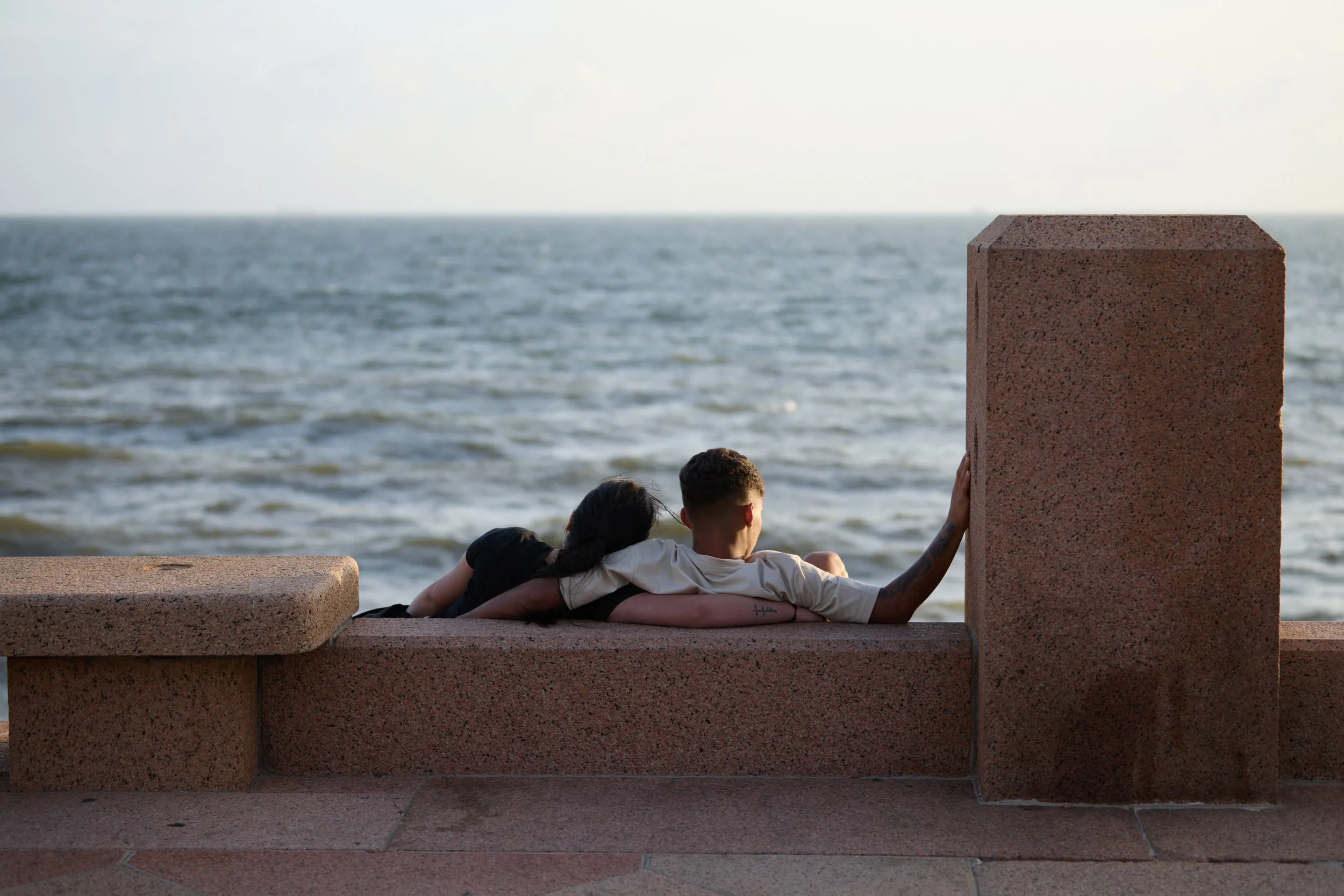 A couple sitting on the rambla parapet, looking out at the river
