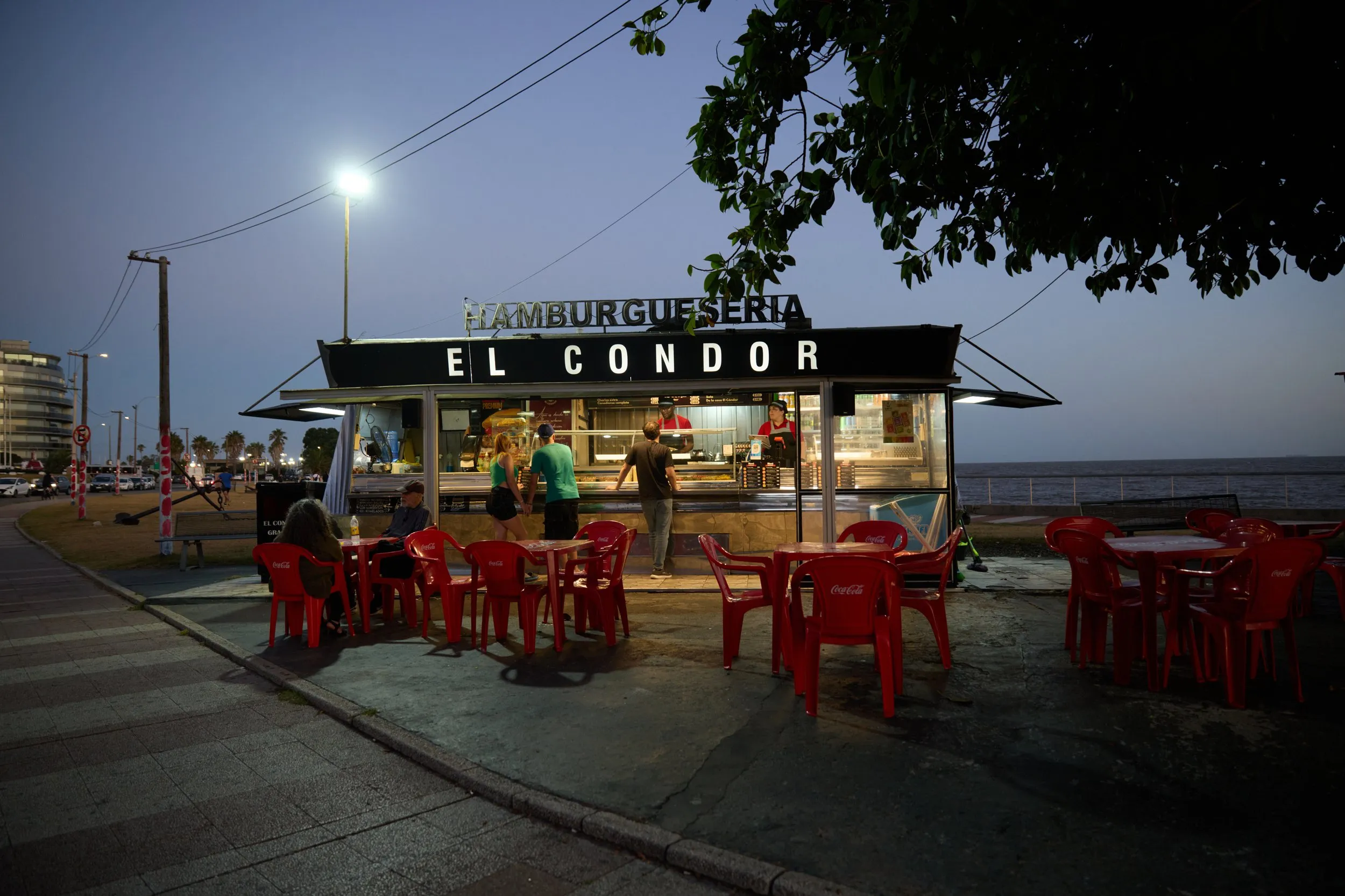 The El Cóndor food stand at night on the Rambla of Montevideo, its red chairs empty