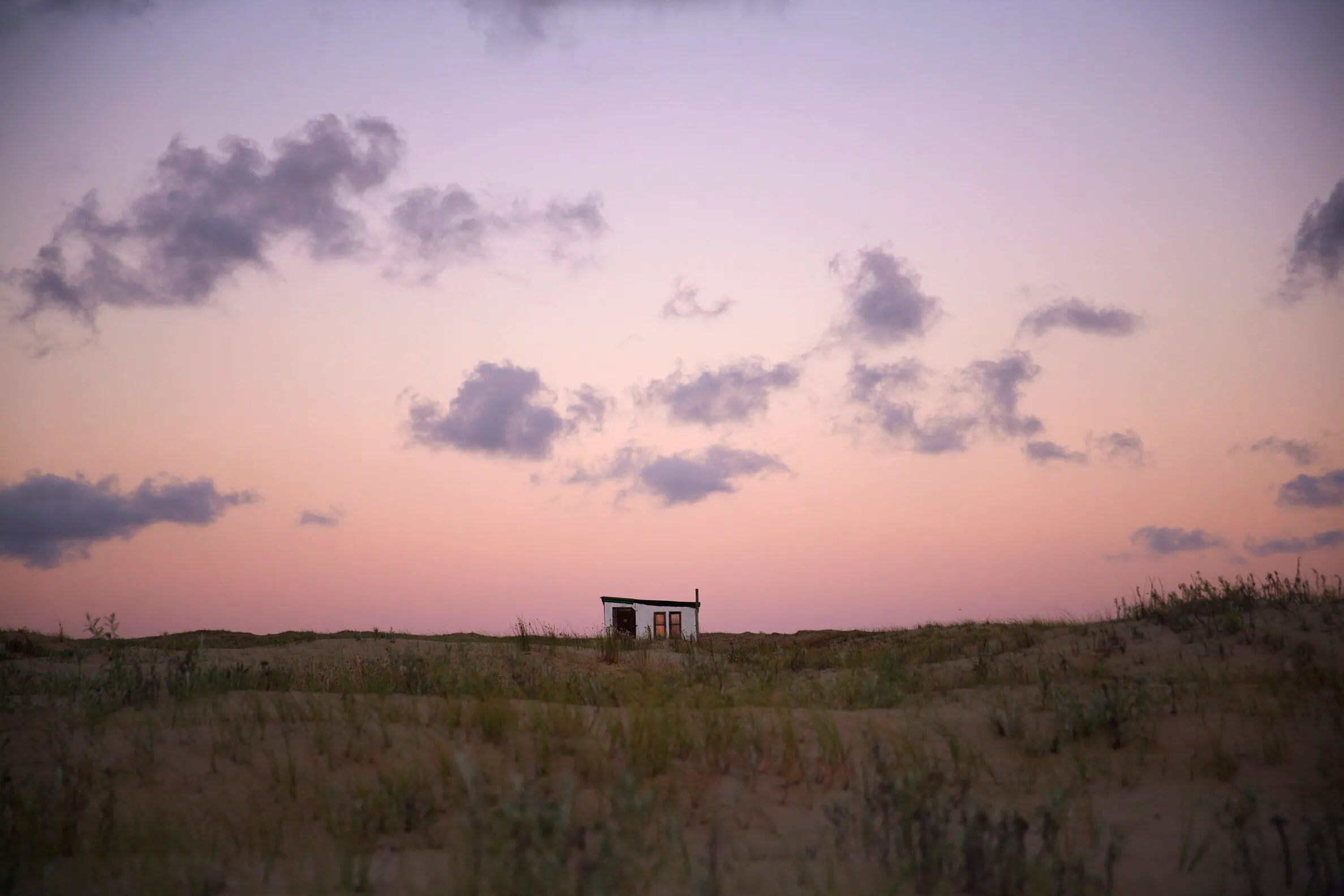 A low ranch house among the grasses of Cabo Polonio, under a lilac sky