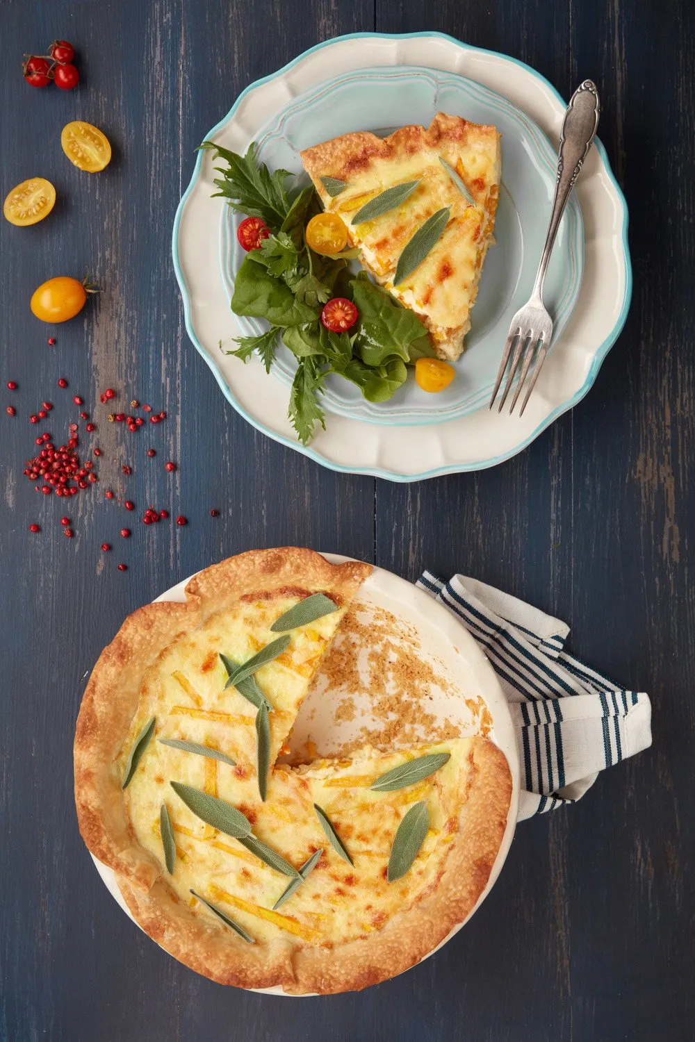 Cheese pizza with sage leaves and a salad of lettuce, yellow tomato, and cherry tomato, with a fork, on a plate with a decorative rim, on a blue wooden table.