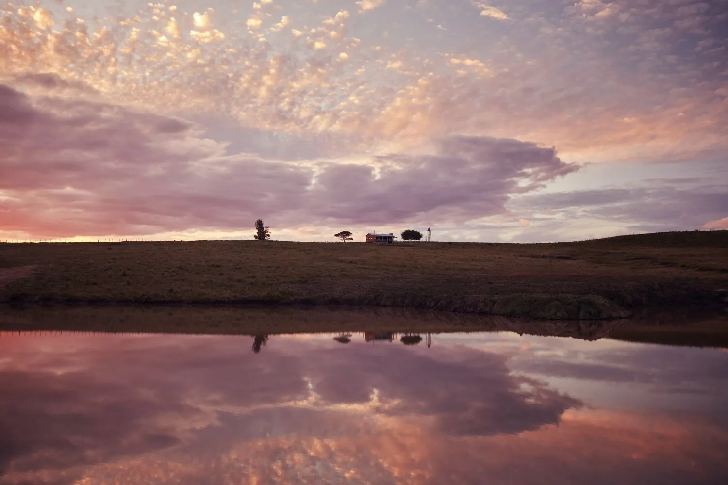 A pink dawn reflected in the water, with a house on the ridge, in Garzón