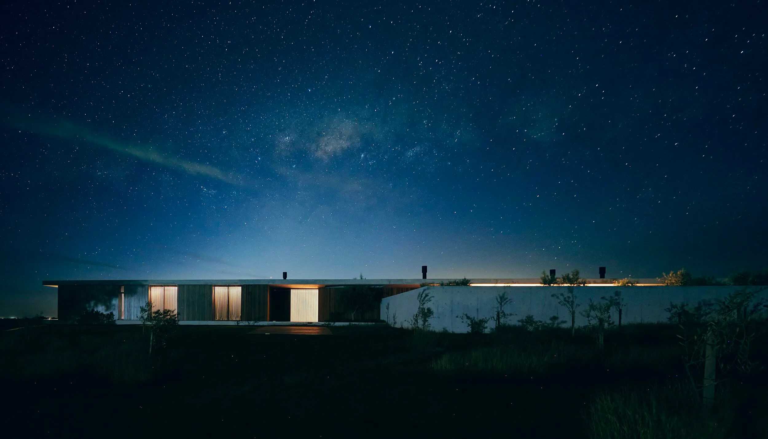 Modern, low-slung building in a dark setting under a clear sky full of stars, with the Milky Way visible.