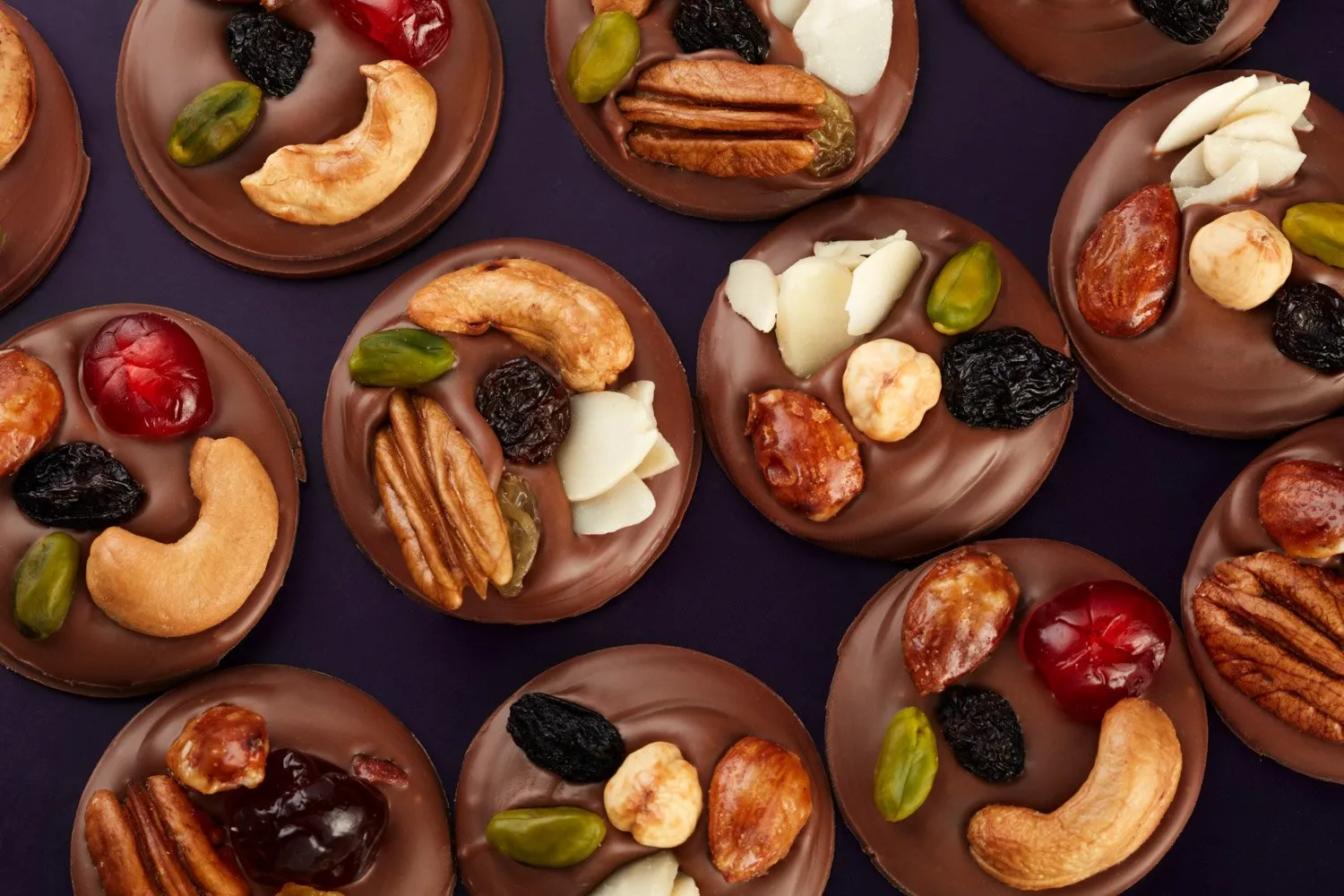 Handmade chocolates decorated with walnuts, almonds, pistachios, raisins, and candied cherries.