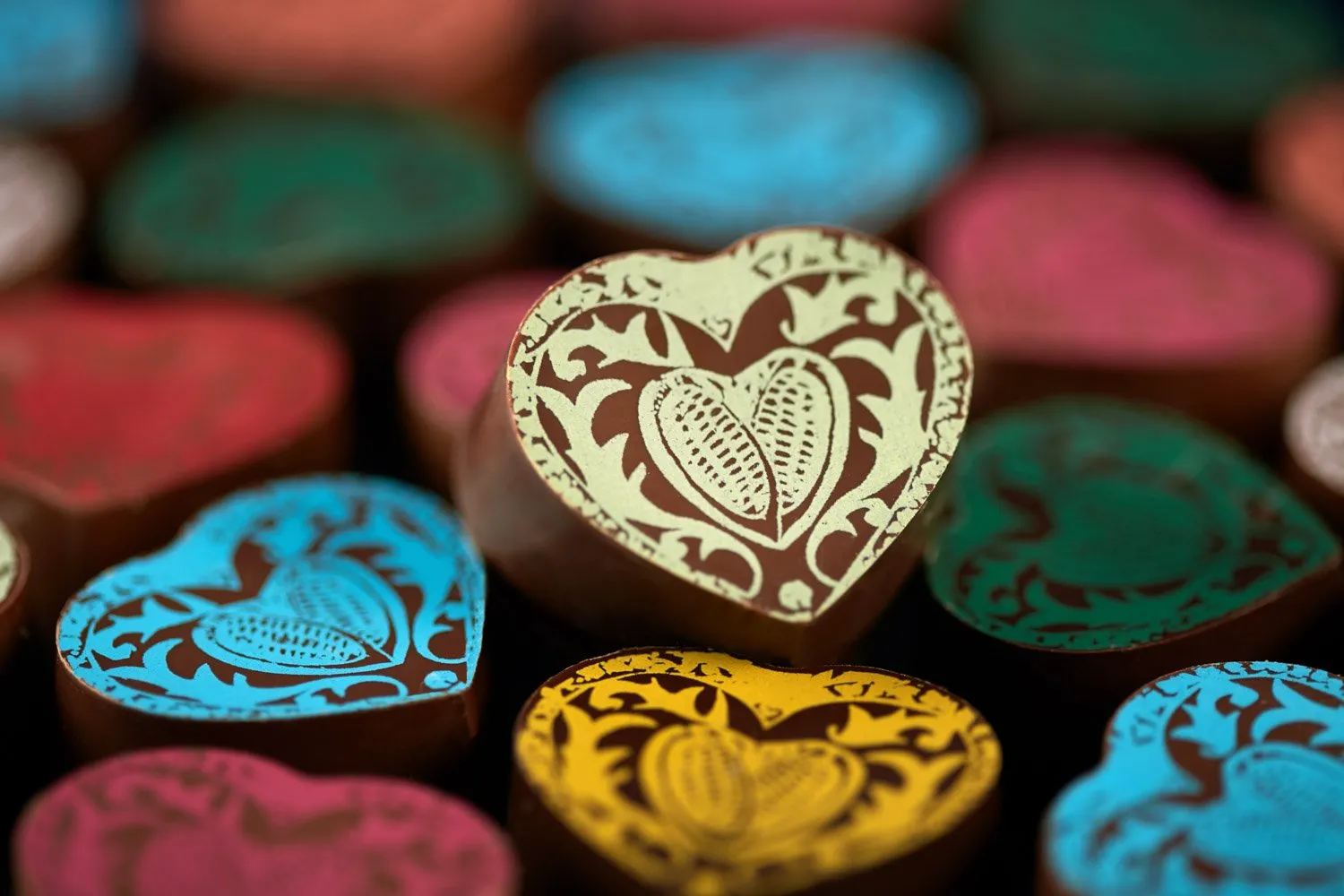 An assortment of chocolate hearts with colorful decorations, with an ornately designed heart in brown and cream tones in the foreground.
