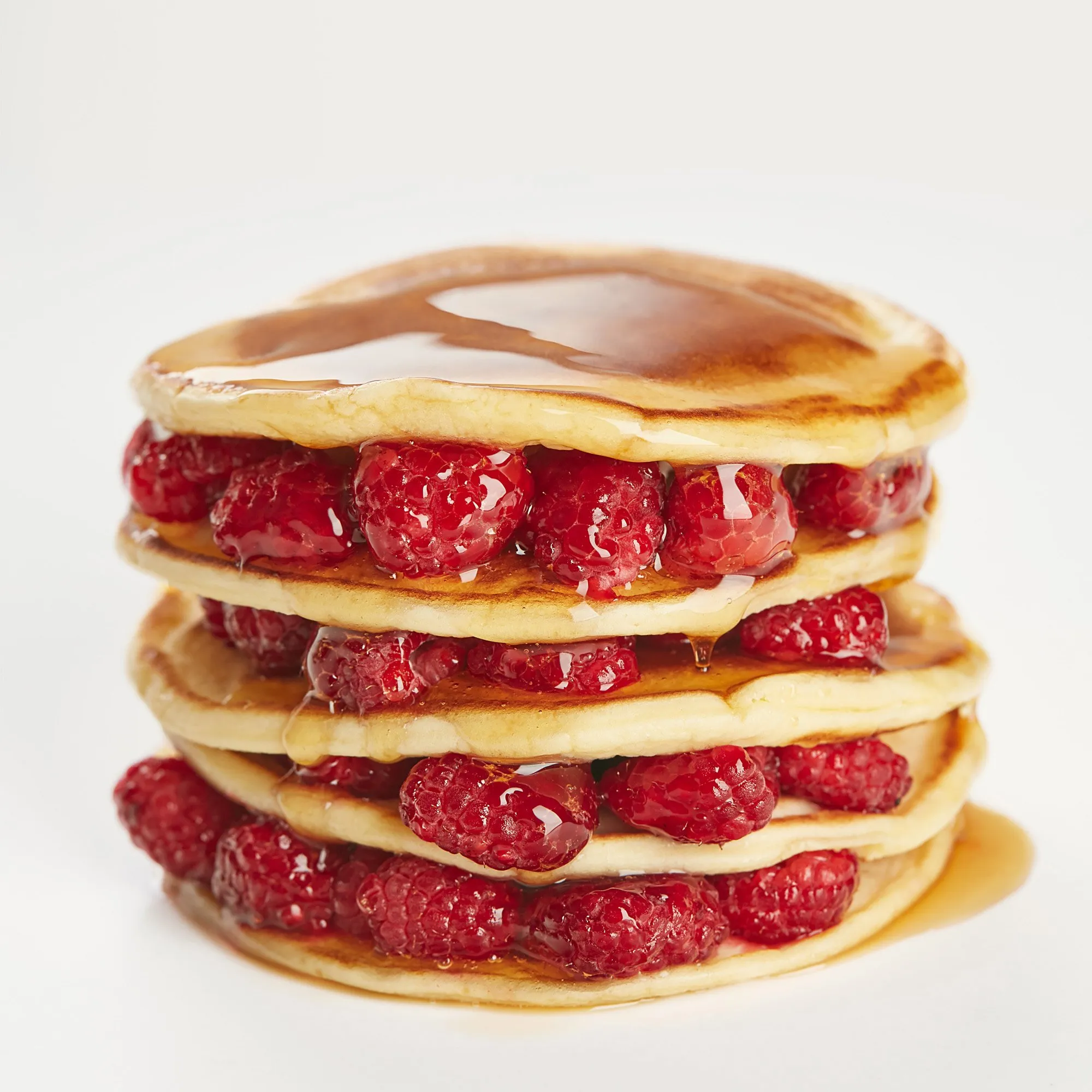 Four stacked pancakes topped with raspberries and syrup.
