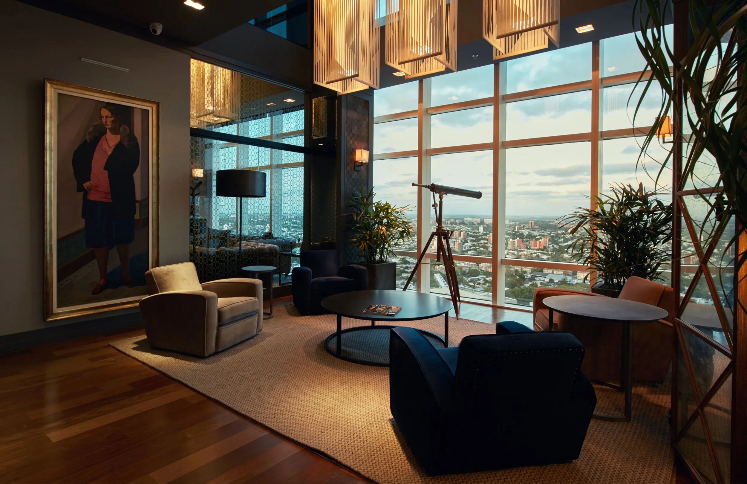 Living room in a high-rise with a city view, armchairs and a coffee table, a telescope beside large windows, and decorative plants.