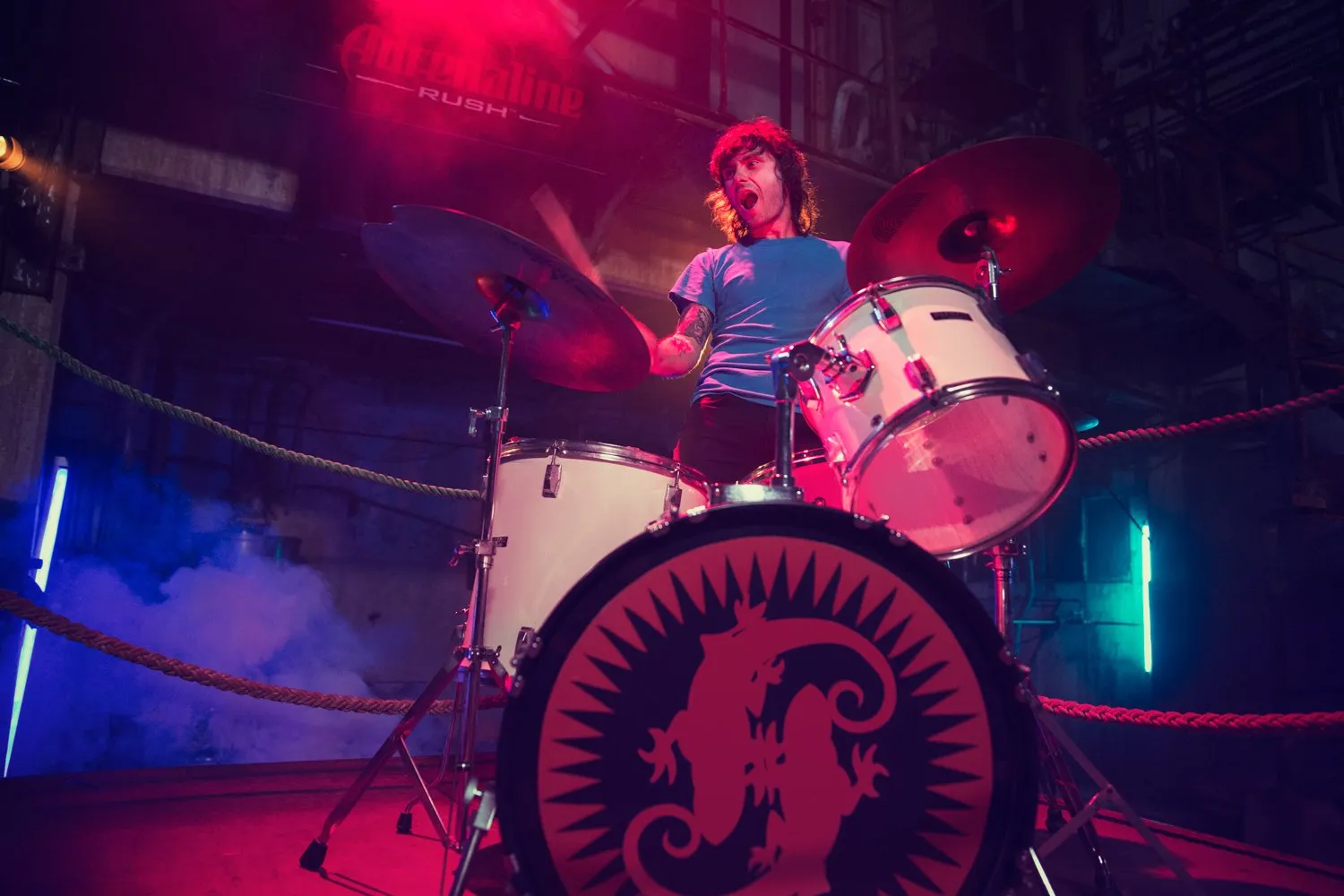 A man playing drums on a stage with colored lights, apparently during a live performance.