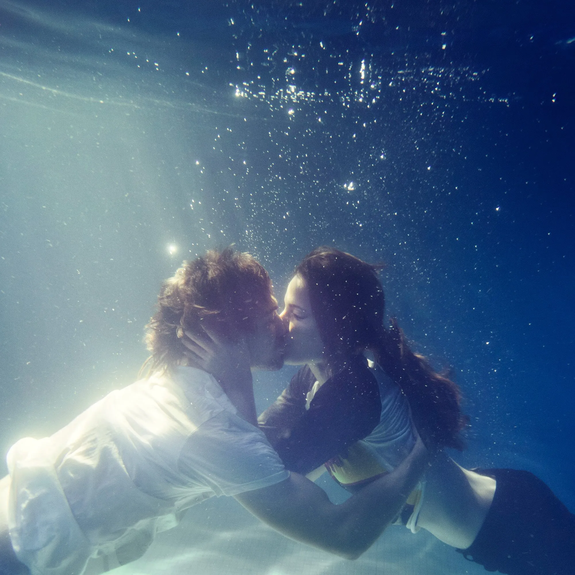 A couple kissing underwater, surrounded by bubbles and light
