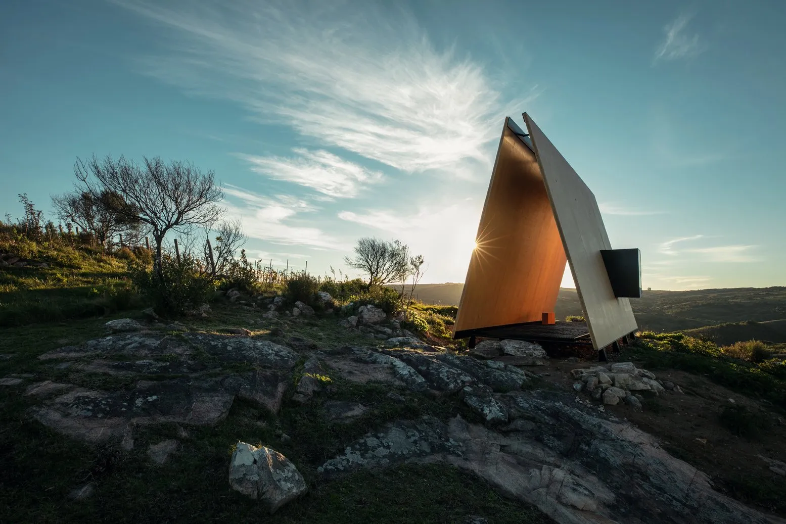 Modern building in a natural landscape with trees and rocks, at sunset with the sun on the horizon.