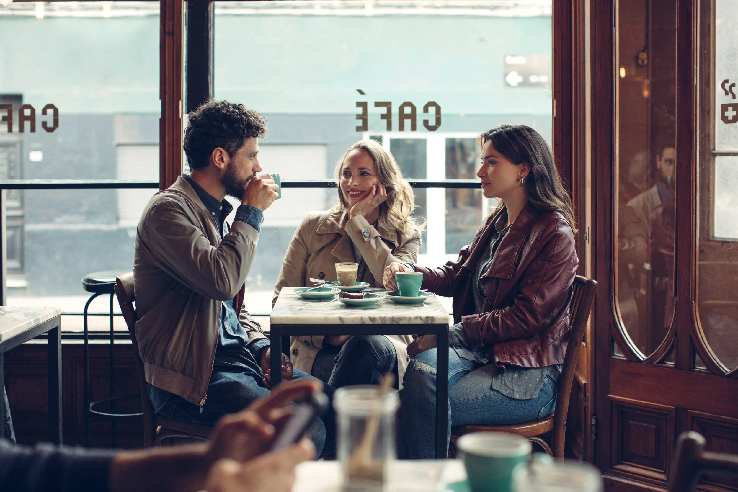 Three people sitting at a café table, talking and drinking coffee.