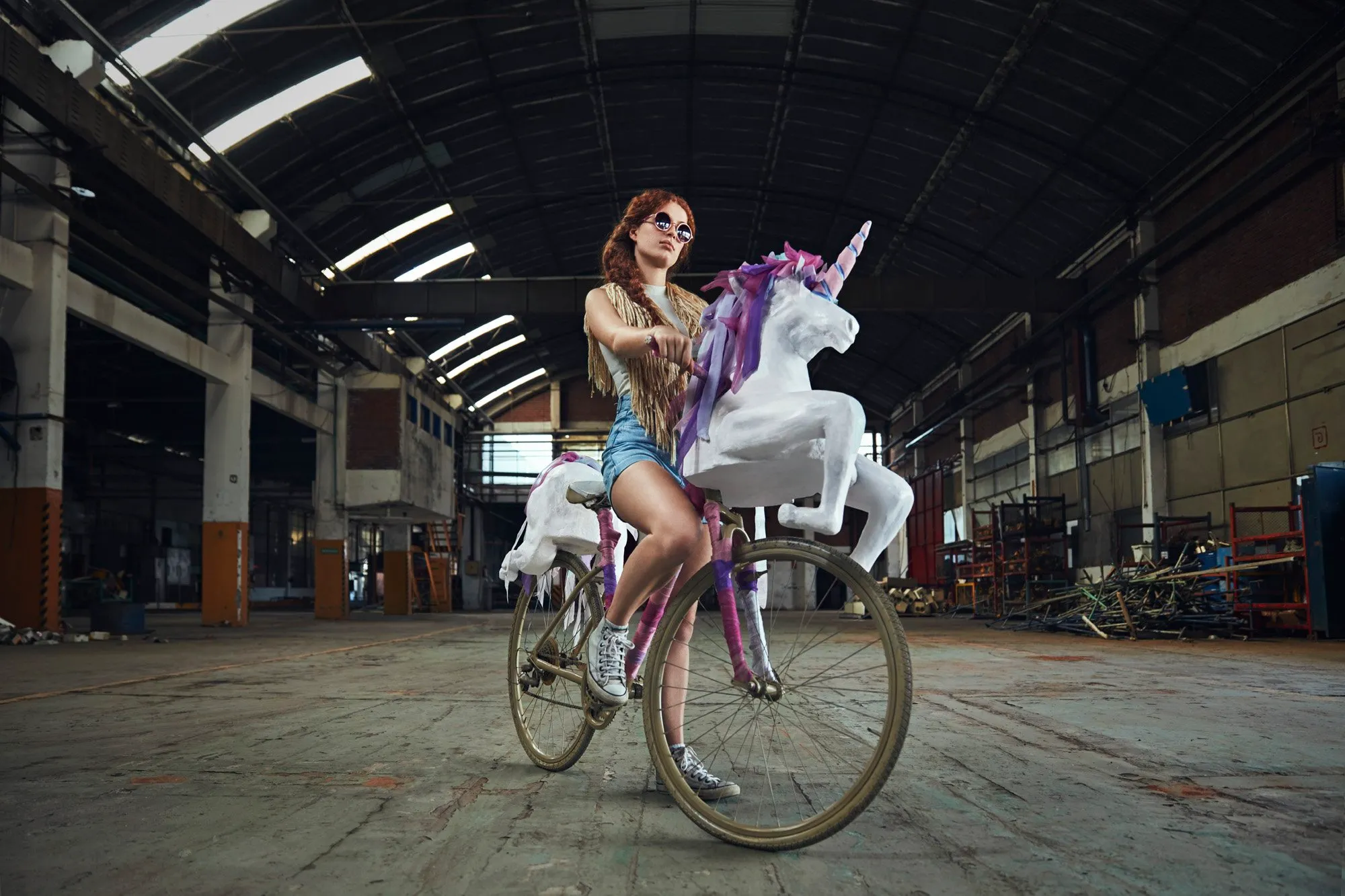A woman riding a bicycle decorated with a unicorn, in an industrial space