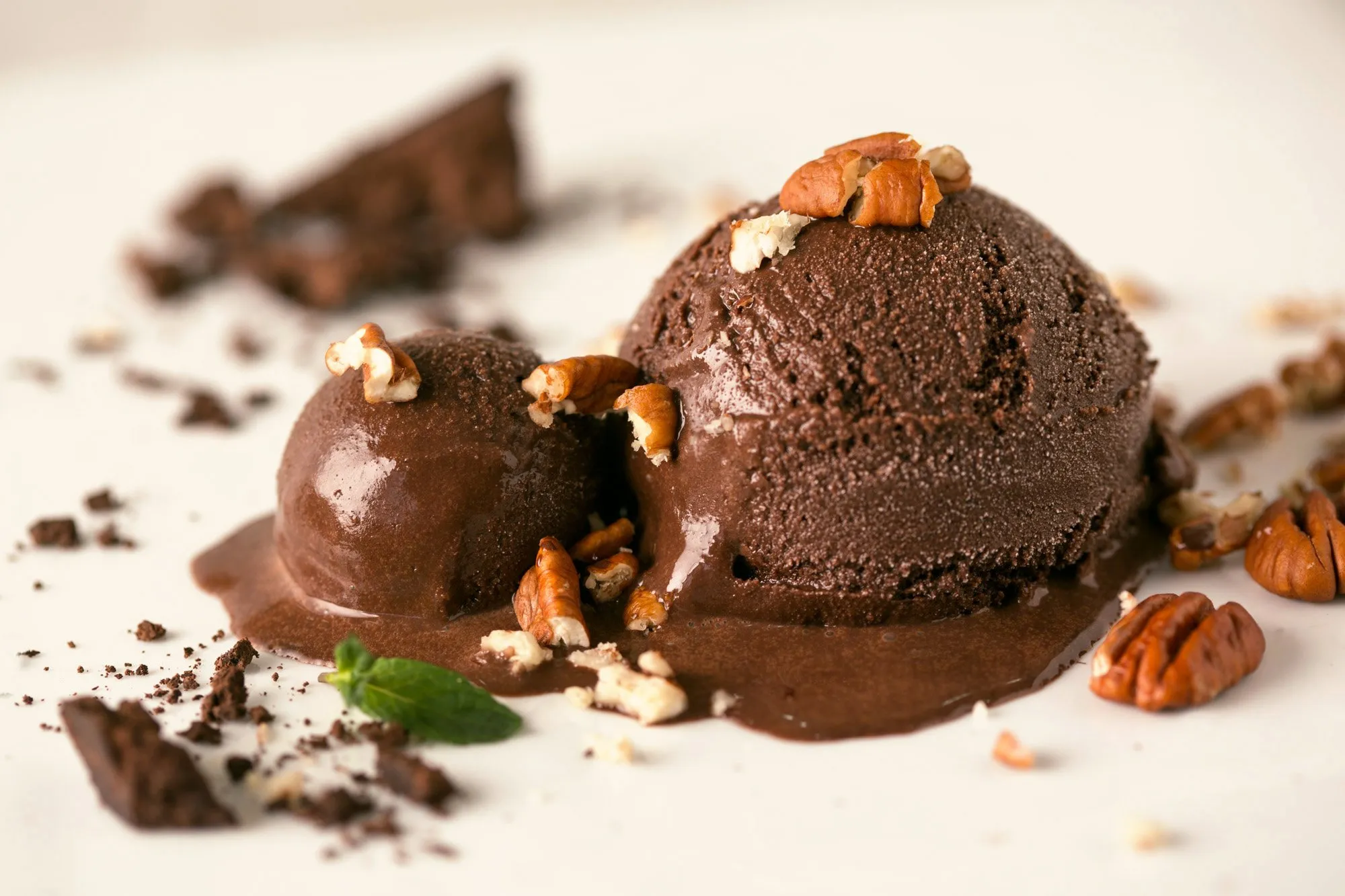 Two scoops of chocolate ice cream topped with chopped nuts and grated chocolate on a white plate.