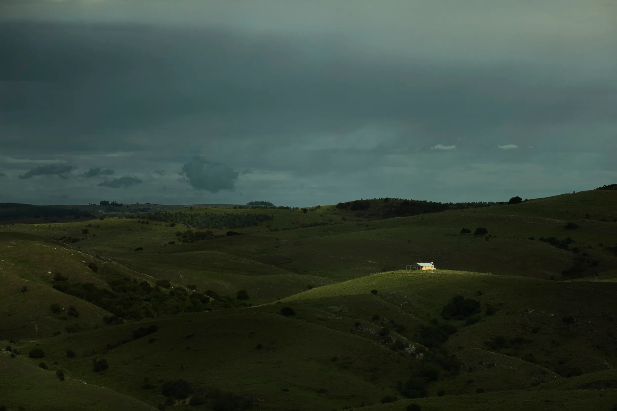 A lone white house among the green hills of Villa Serrana, under a heavy sky