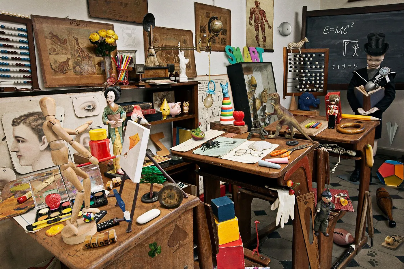 A classroom full of assorted objects, such as puppets, books, toys, scientific instruments, and art supplies, with several tables and walls decorated with pictures, drawings, and educational tools.