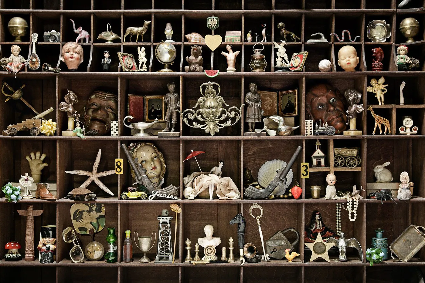 A wooden shelving unit with multiple compartments full of antique and collectible objects, including figures, toys, and assorted ornaments.