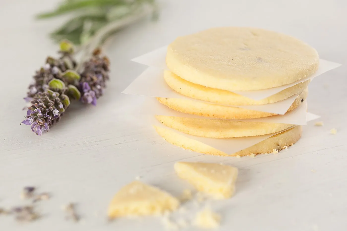 Four cheese-flavored crackers with paper between them, next to lavender flowers and pieces of cheese.