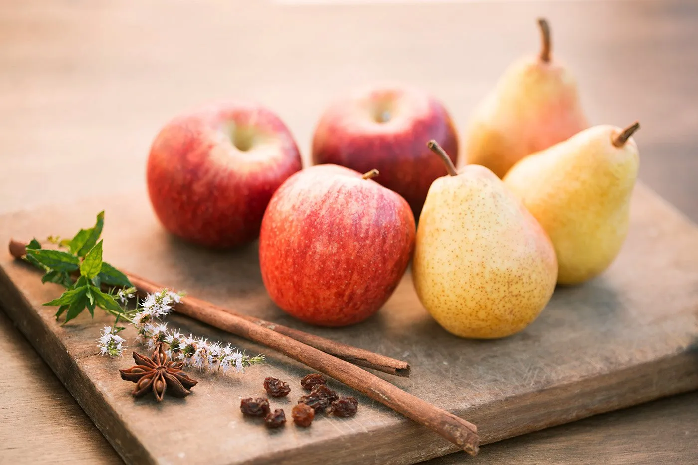 Apples and pears on a wooden board with spices and flowers.