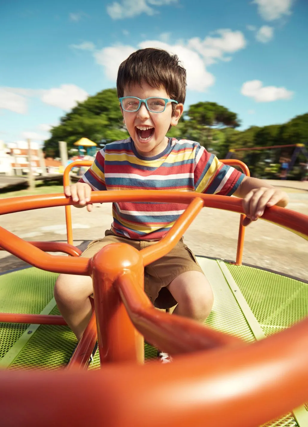 A boy smiling and enjoying himself as he spins on a carousel horse against a background of blue sky and trees.