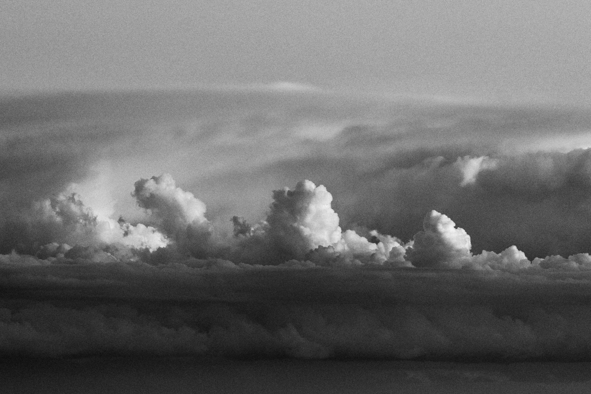 Cumulus piled above a dark band of cloud, in black and white