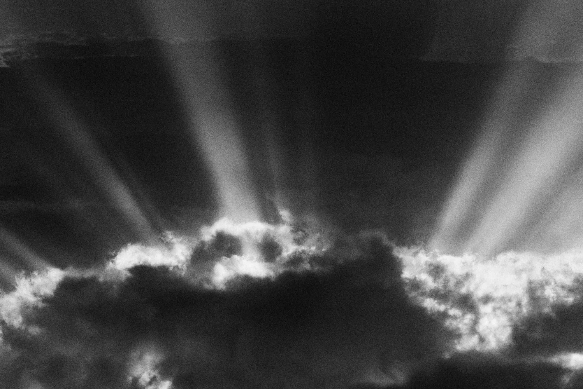 Rays of sun opening above a dark cloud, in black and white