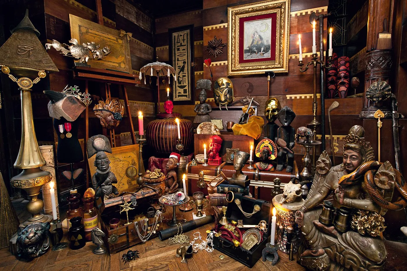 A collection of cultural objects and artifacts, including statues, pictures, and decorative objects in a room with wooden walls.