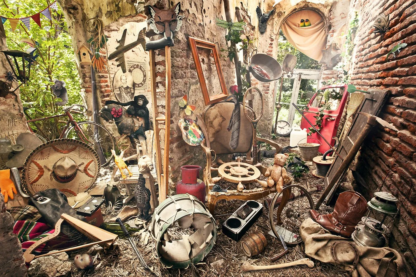 A cluttered interior with old objects and assorted decorations, including a hat, a bicycle, dolls, pictures, plants, and utensils