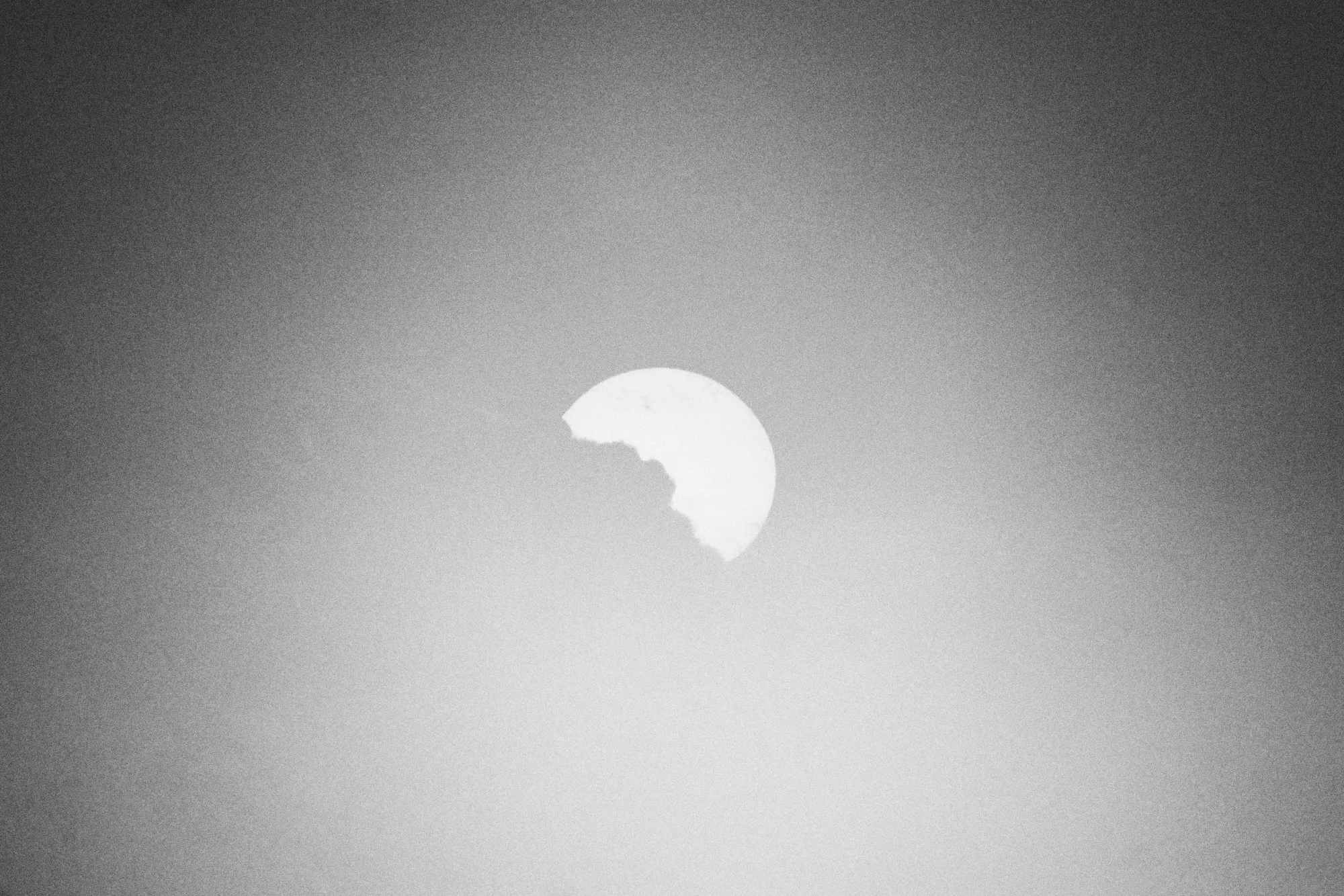 The sun showing from behind a cloud, in a blazing sky, in black and white