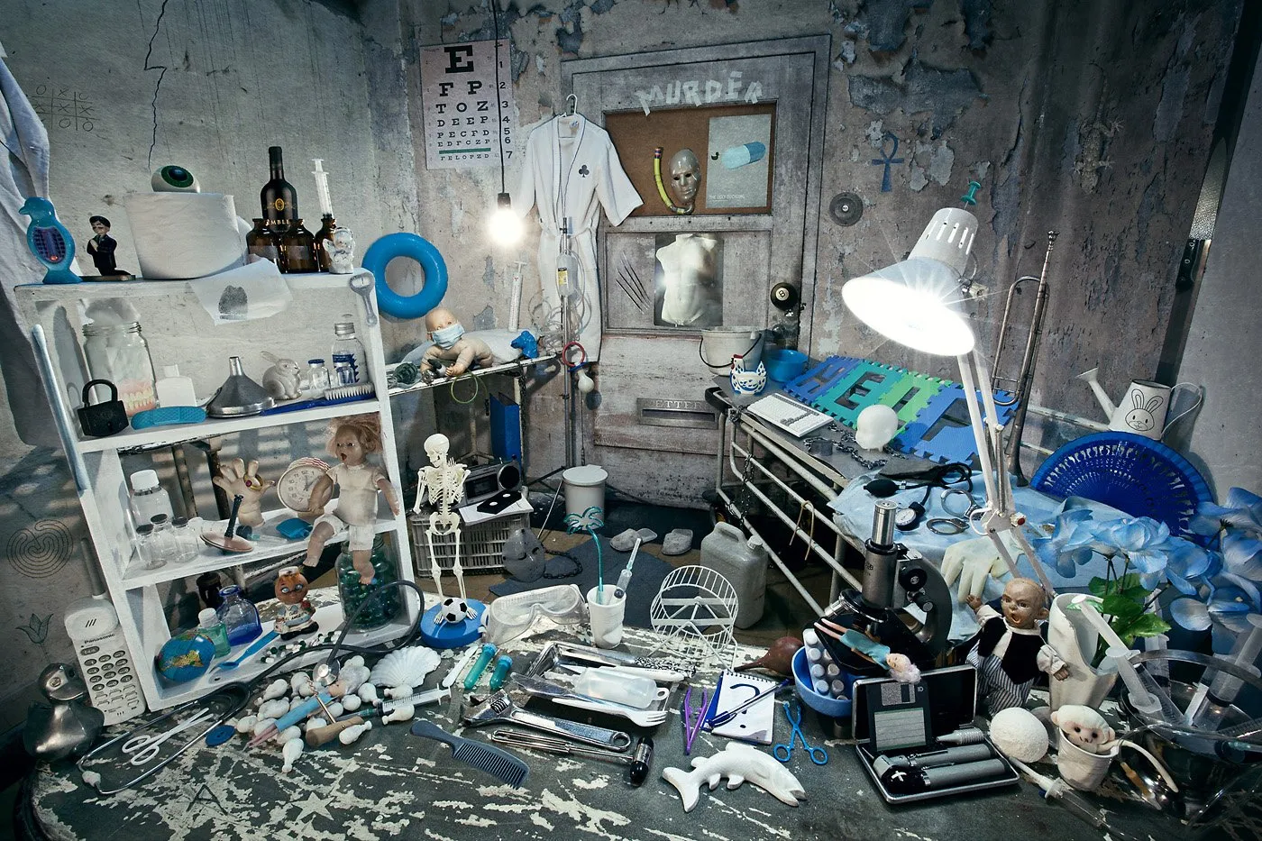 A chaotic space full of assorted objects like dolls, medical instruments, books, a lamp, and office supplies, in a setting that looks like a messy room or an improvised laboratory.